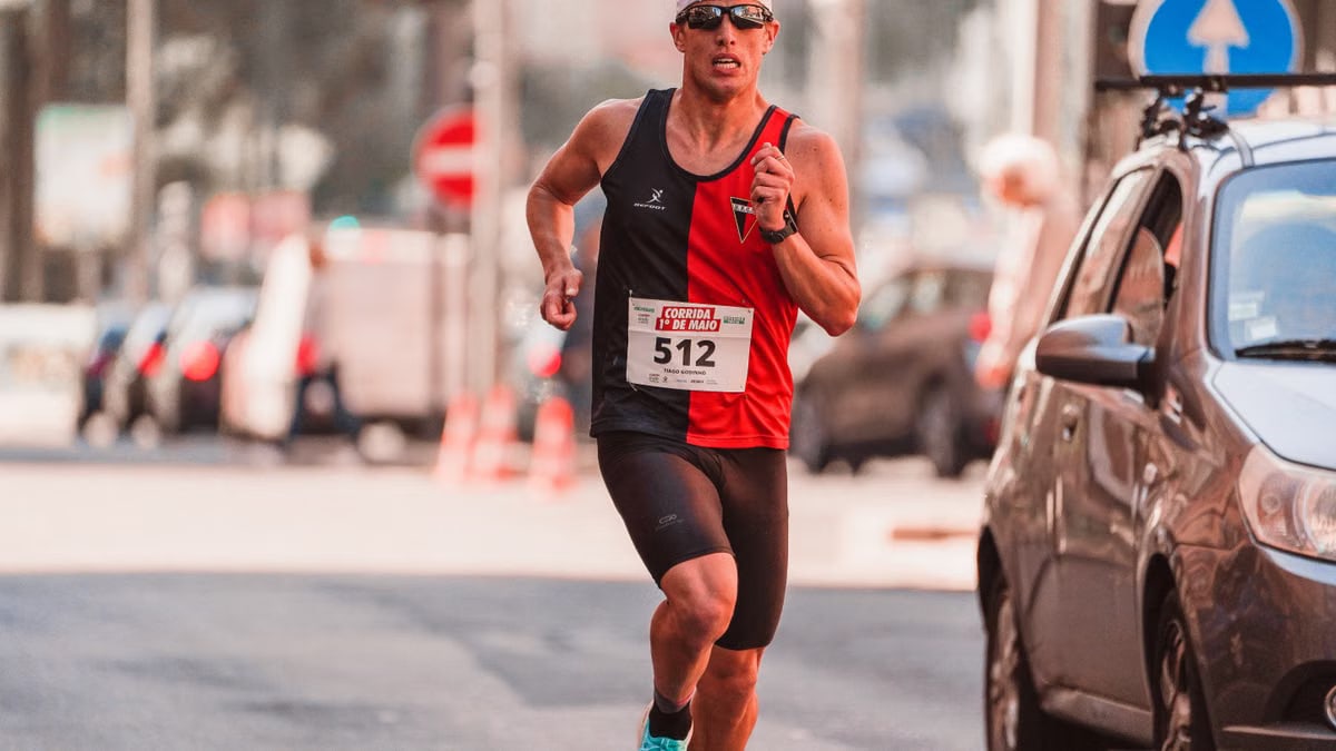 Athletic man wearing a cap and sunglasses competing in a marathon on urban streets.